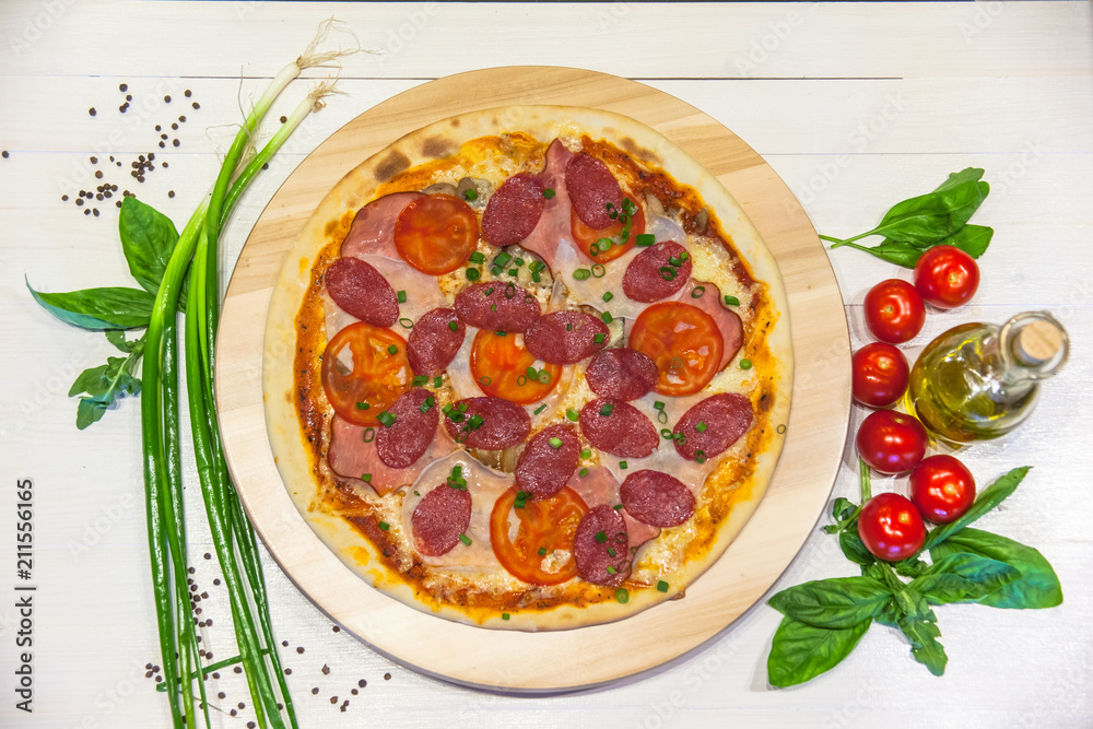 appetizing pizza with sausages and ham, olive oil and basil on a white table, flat lay