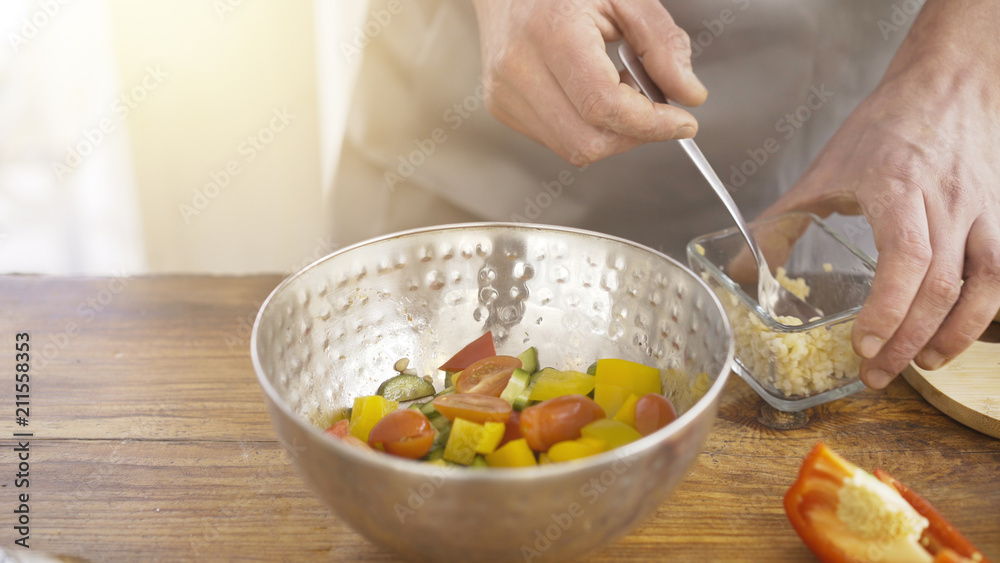 Male cook's hands adding seeds to a salad consisted of cucumbers, paprika and cherry tomatoes in a metal bowl plate