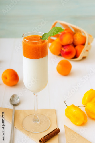 Glass of Panna Cotta, traditional sweet italian dessert, with apricot jelly and touch of yellow hot habanero chilli, cinnamon, decorated with fresh mint.