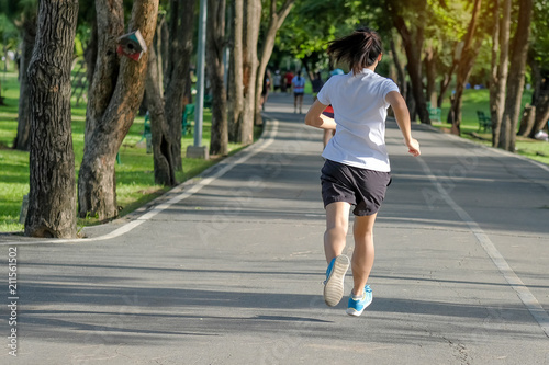 young fitness woman running in the park outdoor, female runner walking on the road outside, asian athlete jogging and exercise on footpath in sunlight morning. Sport, healthy and wellness concepts