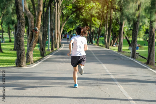 young fitness woman running in the park outdoor, female runner walking on the road outside, asian athlete jogging and exercise on footpath in sunlight morning. Sport, healthy and wellness concepts