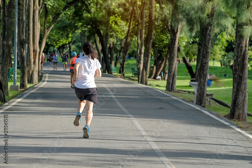 young fitness woman running in the park outdoor, female runner walking on the road outside, asian athlete jogging and exercise on footpath in sunlight morning. Sport, healthy and wellness concepts