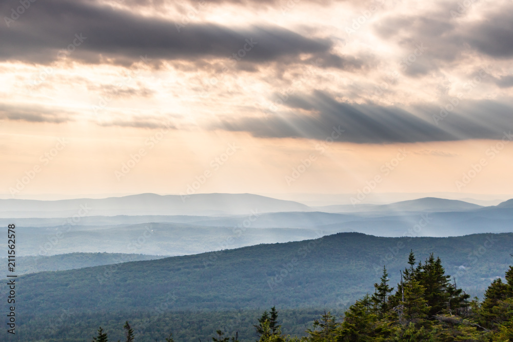 Fototapeta premium Rays of sunlight shining through clouds over rolling mountain view