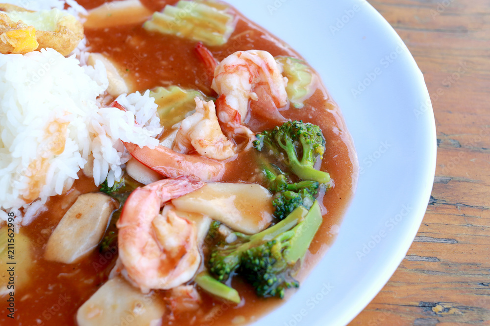 stir fried shrimp and Broccoli in thai red curry paste sauce with rice, Curry fried shrimps and cooked rice in white dish closeup on wooden table. Thai style food. stir fried shrimp and Broccoli in thai red curry paste sauce with rice, Curry fried shrimps and cooked rice in white dish closeup on wooden table. Thai style food.