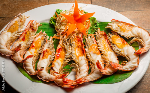 Grilled shrimp with Shrimp Paste in white dish showing the delicious Shrimp Paste inside its shell on wood table. Thai seafood.