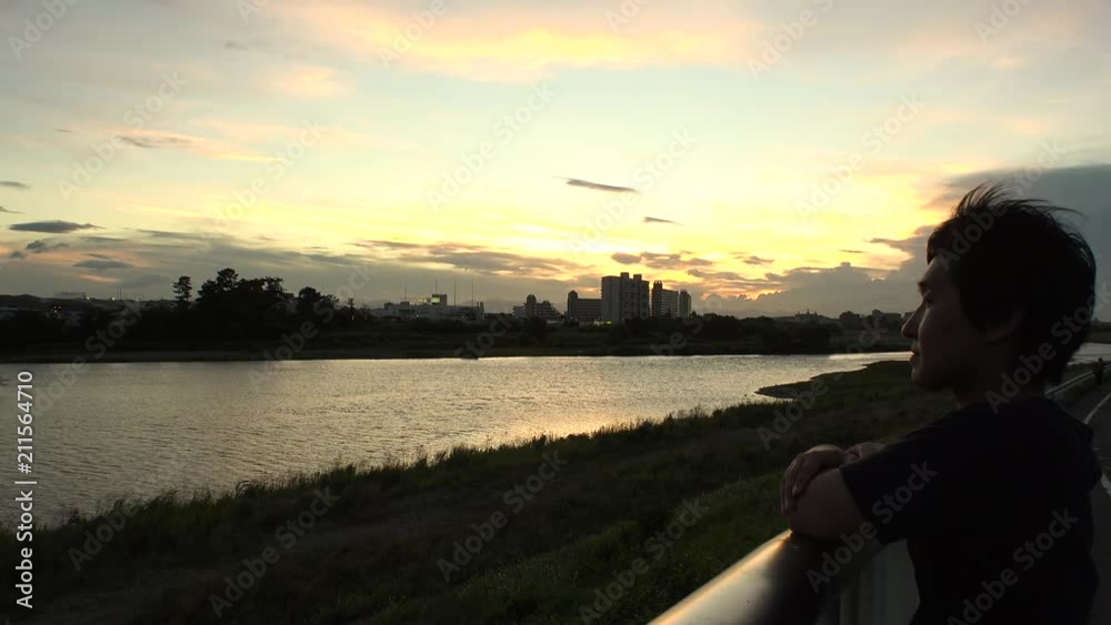 Young JAPANESE MAN looking at the river and thinking of something.  At sunset riverside of Tama river in Tokyo.
