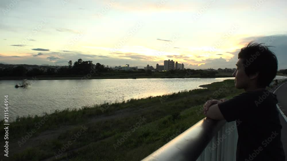 Young JAPANESE MAN looking at the river and thinking of something.  At sunset riverside of Tama river in Tokyo.