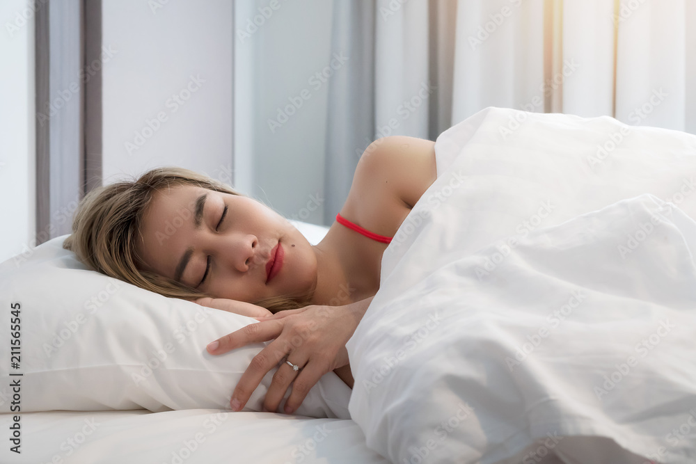 Asian young smiling pretty lady lies in bed indoors. Eyes closed. Asian young smiling pretty lady lies in bed indoors. Eyes closed.