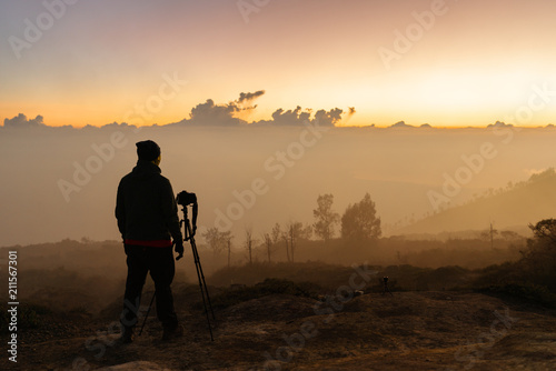 Photographer with camera and tripod waiting sunrise on the mountain peak