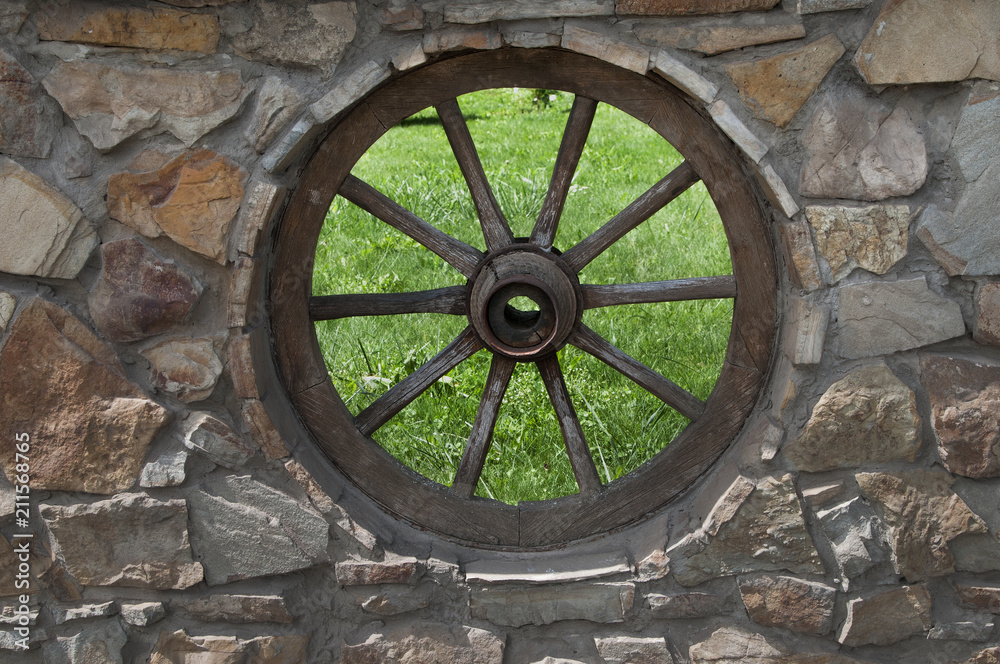 The vintage wheel in the wall made of stones as decoration