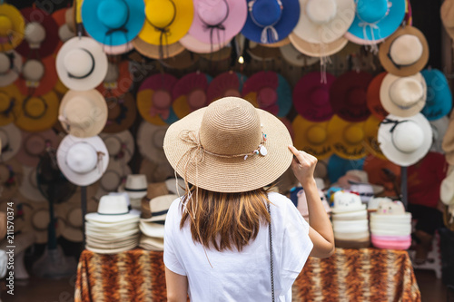 Young woman traveler looking for hat at the local market in Thailand