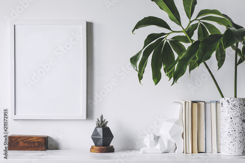Scandinavian interior with white cupboard, mock up poster frame, cat figures, tropical leaf and books. Modern and minimalistic concept of space. photo