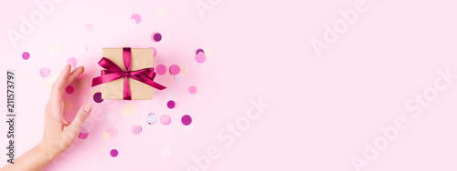 Woman hand and kraft gift box with pink bow on pink background decorated with...