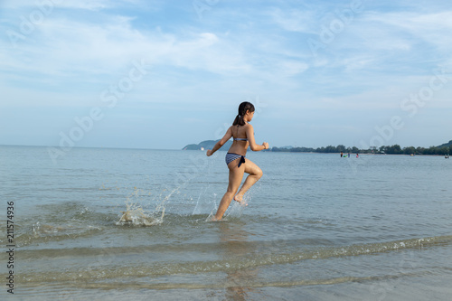 Teenage wearing bikini running at the beach by the sea.