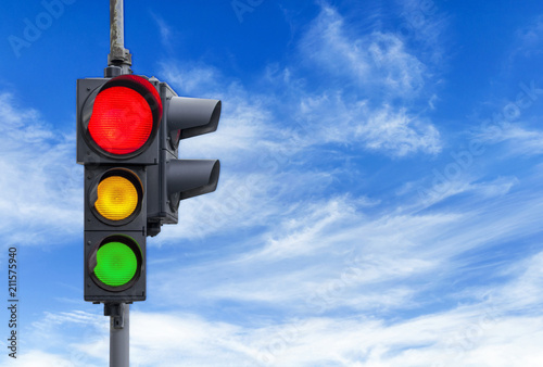 Red semaphore light with yellow and green and cloudy sky background