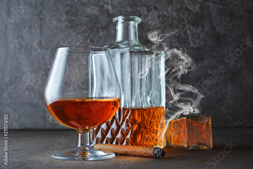 Strong alcoholic drink cognac in sniffer glass and crystal decanter with smoking cigar