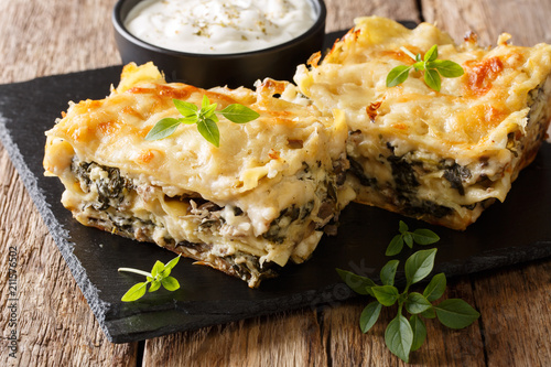 Casserole of lasagna with chicken breast, wild mushrooms, cheese, herbs and bechamel sauce close-up on a slate plate on a wooden table. horizontal