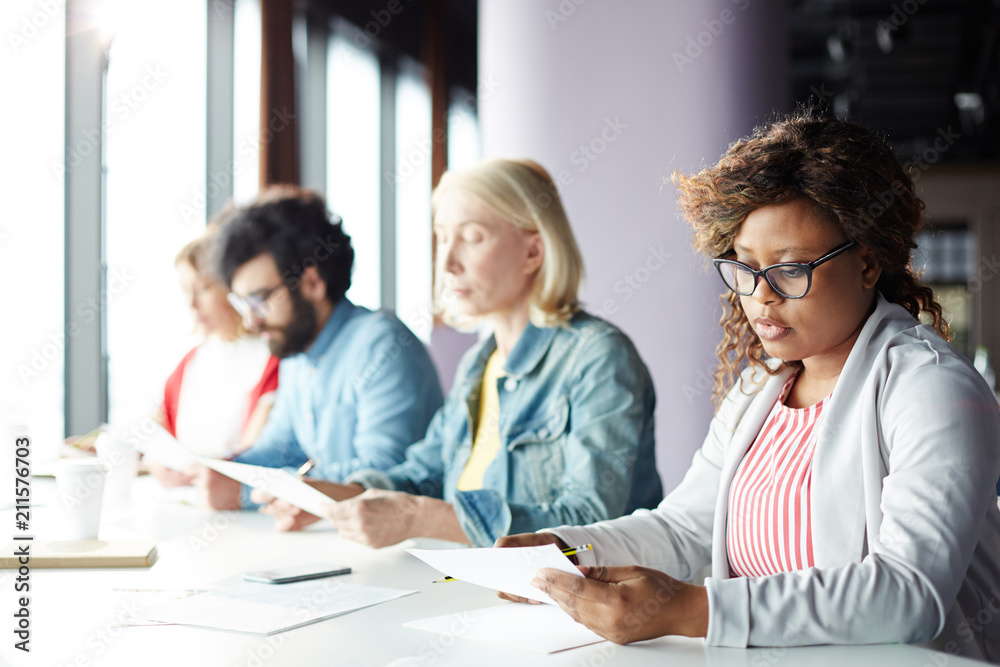 Serious businesswoman concentrating on reading important document on background of colleagues Serious businesswoman concentrating on reading important document on background of colleagues
