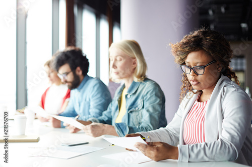 Serious businesswoman concentrating on reading important document on background of colleagues