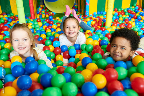 Colorful portrait of three happy kids smiling happily at camera while having fun in ball pit of children play center, copy space