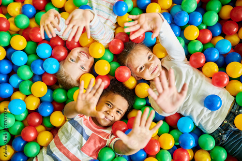 Above view portrait of three happy little kids in ball pit smiling at camera ...
