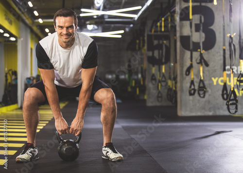 Full length portrait of cheerful man keeping sports equipment while working out in gym