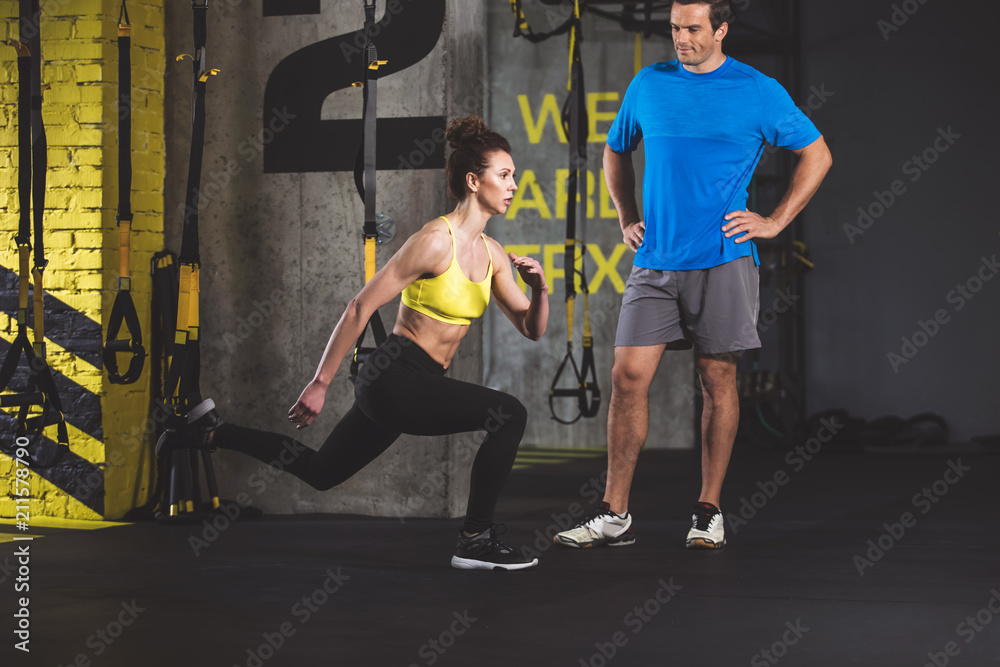 Full length concentrated female instructor showing lunges. Serene man looking at her Full length concentrated female instructor showing lunges. Serene man looking at her