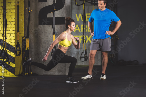 Full length concentrated female instructor showing lunges. Serene man looking at her