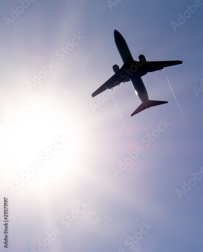 The plane flies in the sky against the sun. 