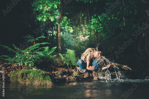 Young hiking lady washing her hands in the fresh cool water of a mountain stream.