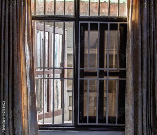 A barred window open to the street  in close is wall of the next house.