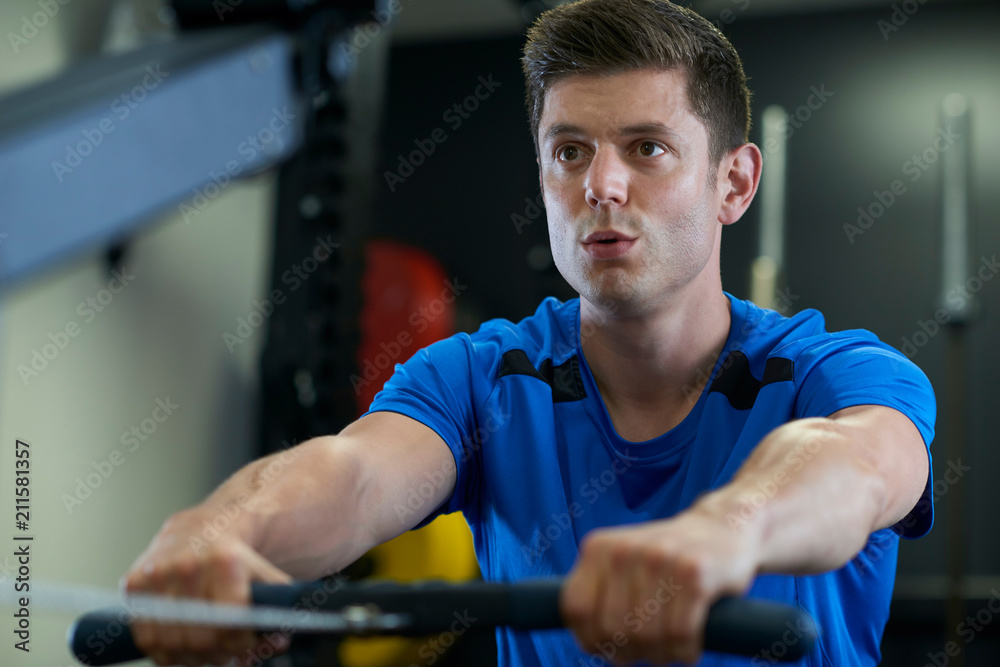 Fototapeta premium Man In Gym Exercising On Rowing Machine