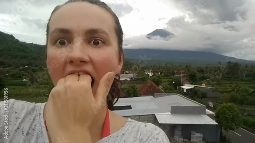 woman making selfie on cell phone, making scared face, agung Volcano erupting january 2018 photo