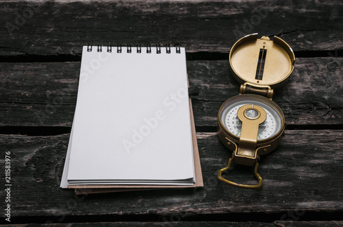 Compass and blank page notepad on old wooden table background.