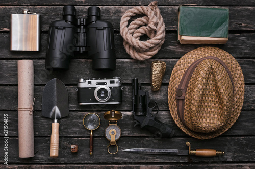 Compass, binoculars, film photo camera, loupe, dagger, handgun, diary book, shovel, rope, gold ore and old scroll document on adventurer or explorer wooden table. Traveler.
