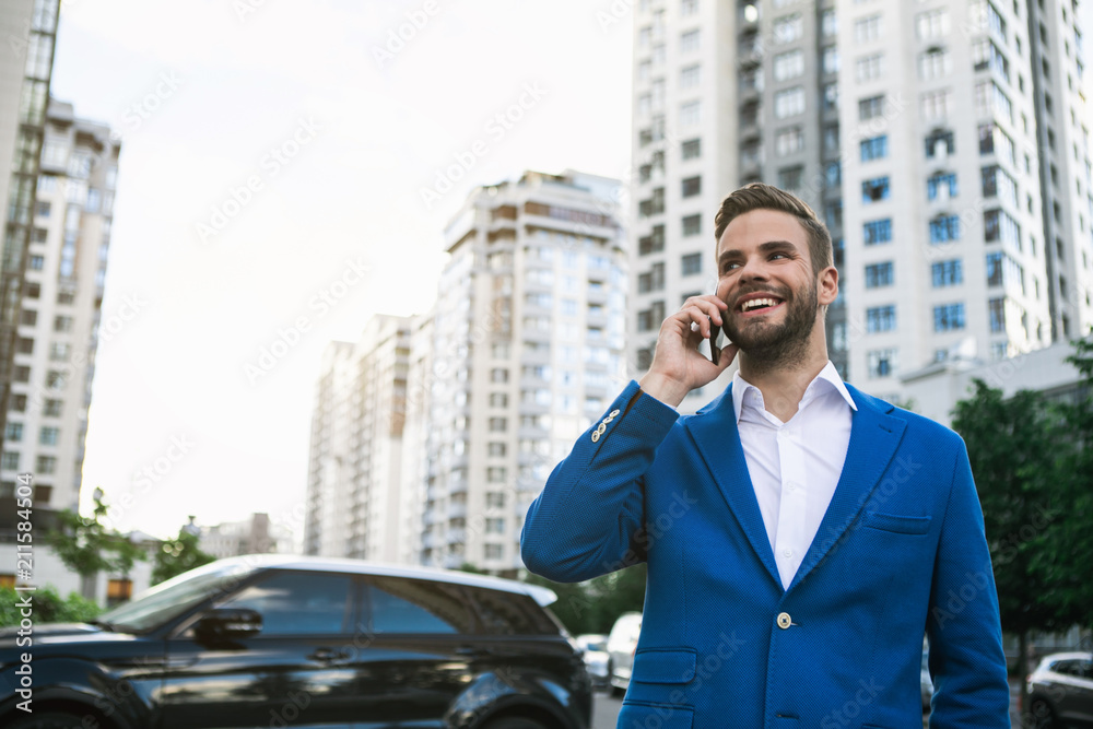 Portrait of successful male manager talking on mobile phone with joy. He is standing on street and laughing. Copy space Portrait of successful male manager talking on mobile phone with joy. He is standing on street and laughing. Copy space