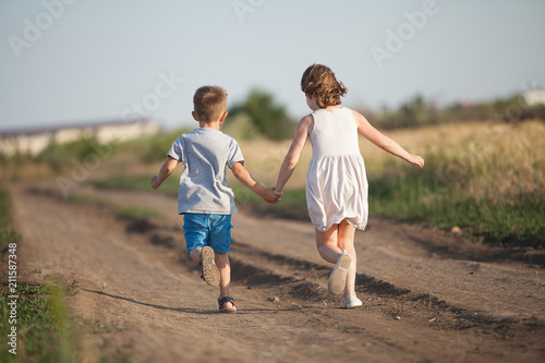  A boy and girl holding hands amicably running across the field in the summer