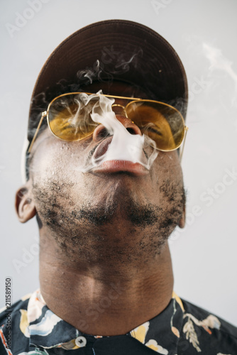 Black stylish man wearing sunglasses. He is vaping with an electronic cigarrete outdoor photo