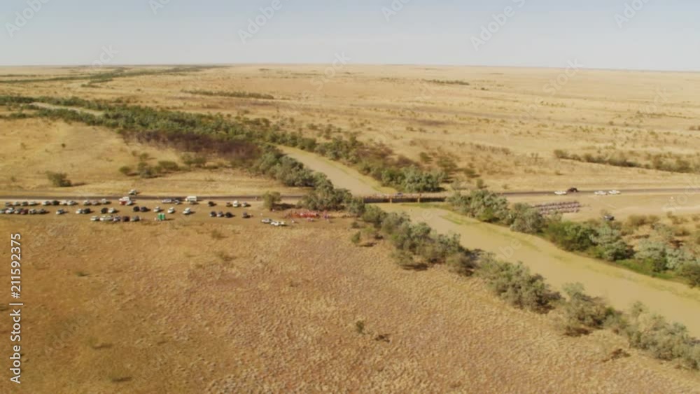 An aerial shot of trees and land with cars in slow motion. Camera slowly moves backward.