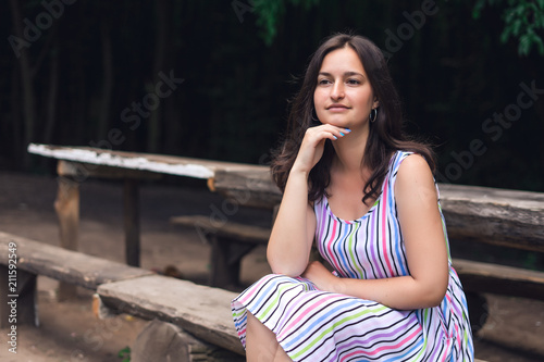Young woman sitting on bench in summer forest.