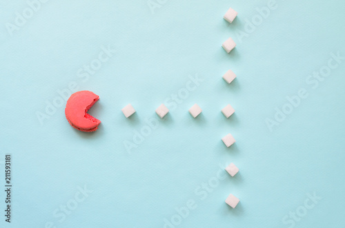 A composition of macaroon with an open mouth that is going to eat sugar cubes on a blue pastel background. The concept of old video games photo