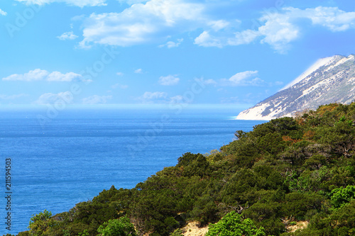 Sea shore landscape - green mountains with forest on the blue cloudy sky background