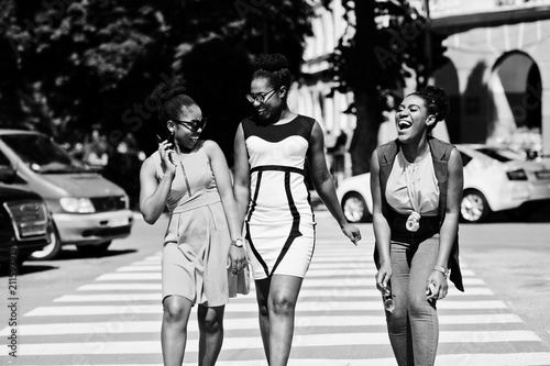 Three stylish african american womans walking on crosswalk or pedestrian crossing, speaking each other and having fun.