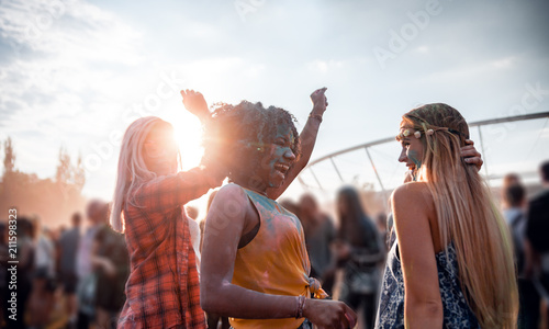 Multiethnic girls covered in colorful powder dancing and celebrating summer holi festival