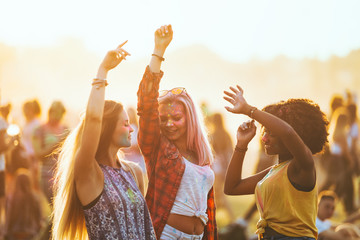 Multiethnic girls covered in colorful powder dancing and celebrating summer holi festival