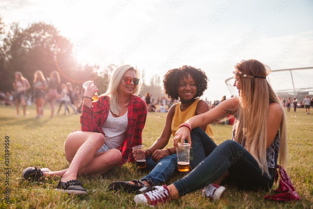 Group of multiethnic friends drinking beer ang sitting together at summer music festival