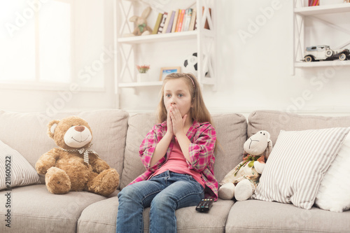 Shocked little girl watching tv sitting on sofa