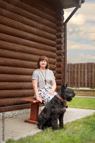 Fotografie an elderly woman is sitting on a village bench with a black schnauzer near a woo