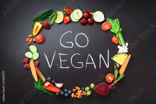 Healthy food background. Circle of fresh vegetables, fruits, nuts, berries with handwritten phrase Go Vegan on black chalkboard. Top view. Vegetarian, vegan, detox and clean eating concept