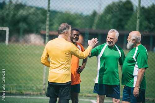 interracial elderly football players shaking hands after match on green field